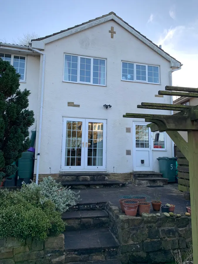 A white-painted two-storey house with a pergola over the rear patio