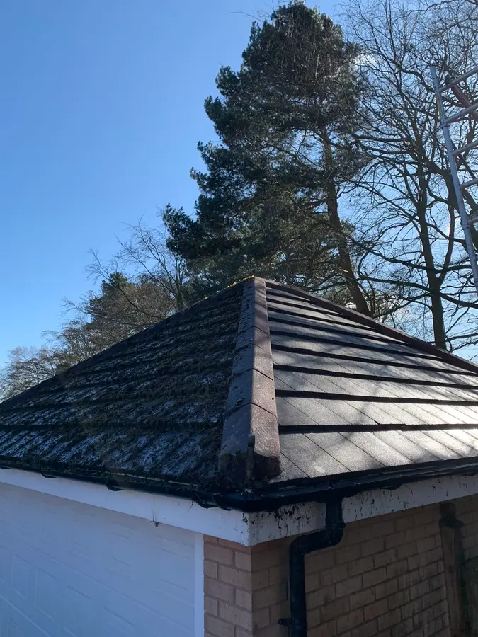 A cleaned dark-tiled hipped roof on an outbuilding against a clear sky