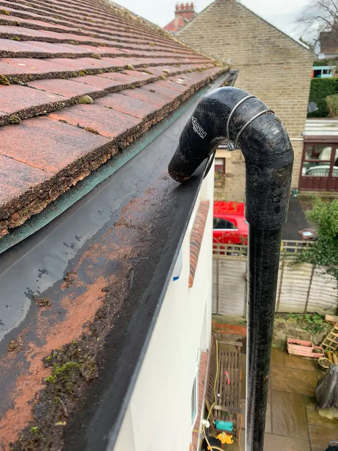 A roof edge, gutter and black downpipe hopper seen from roof level